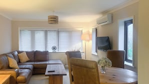 A living room with a brown leather sofa, a wooden coffee table, a round wooden table, and a TV mounted on the wall. - 2 bedroom accommodation in Clanfield, near Petersfield (Clanfield, near Petersfield)