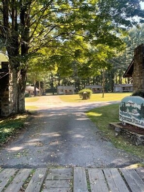 A paved pathway leading to a rustic building with a sign reading "Pioneer Village."