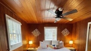 A bedroom with wooden walls and ceiling, a bed with white bedding, two bedside tables with lamps, and a ceiling fan.