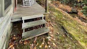 A rustic cabin with a wooden porch, a rocking chair, and a stone wall.