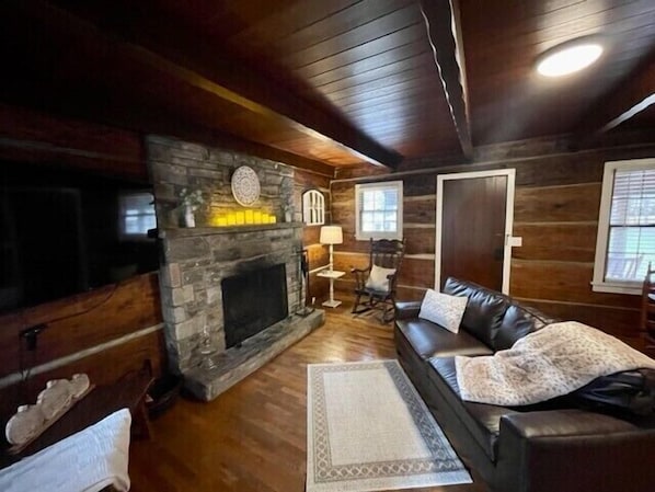 L’intérieur d’une cabane en rondins, avec une cheminée en pierre, un canapé en cuir et un plancher en bois.