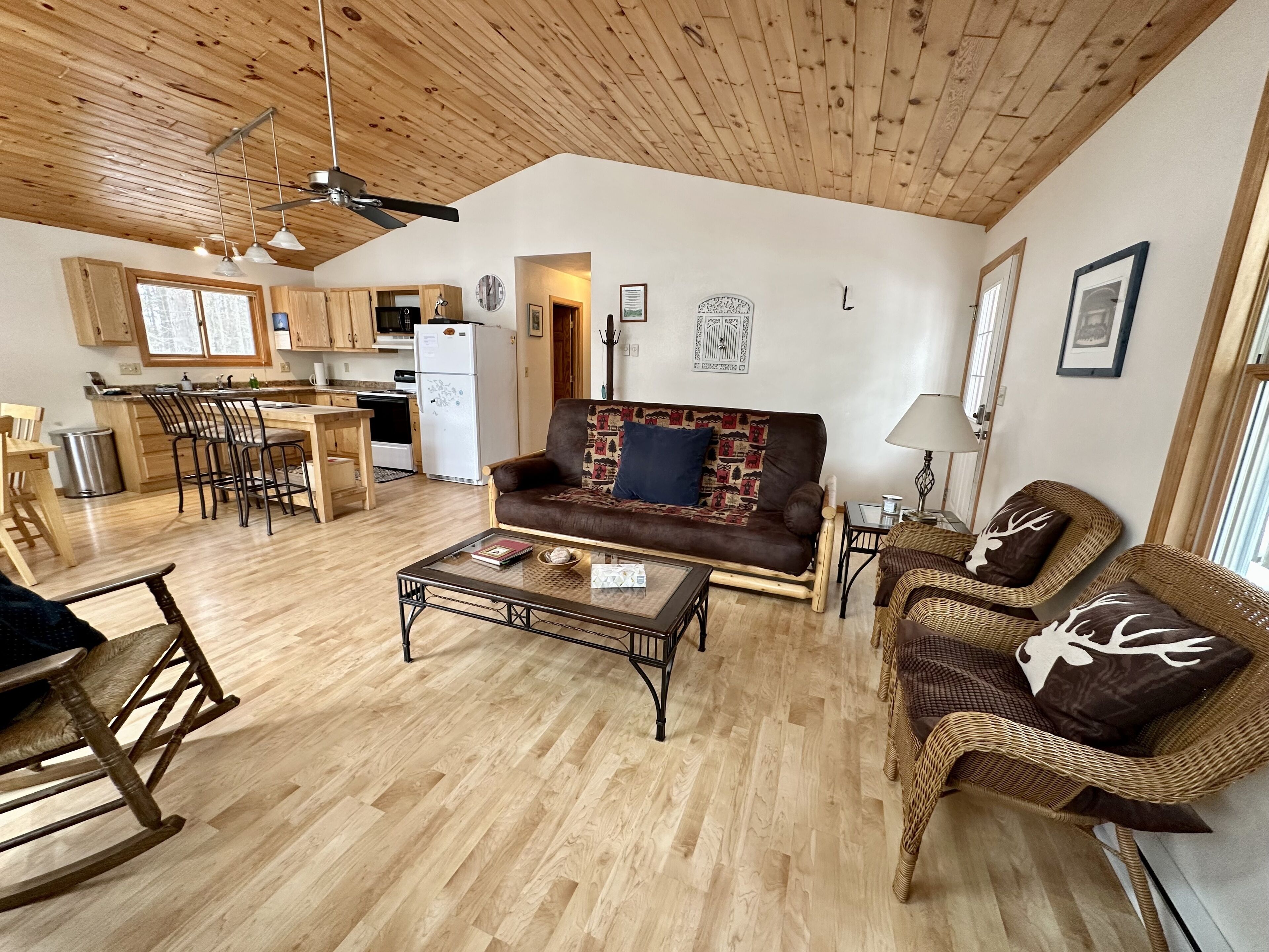 Ett rymligt vardagsrum med ett träpanelat tak, en soffa, ett soffbord och fåtöljer i rotting.