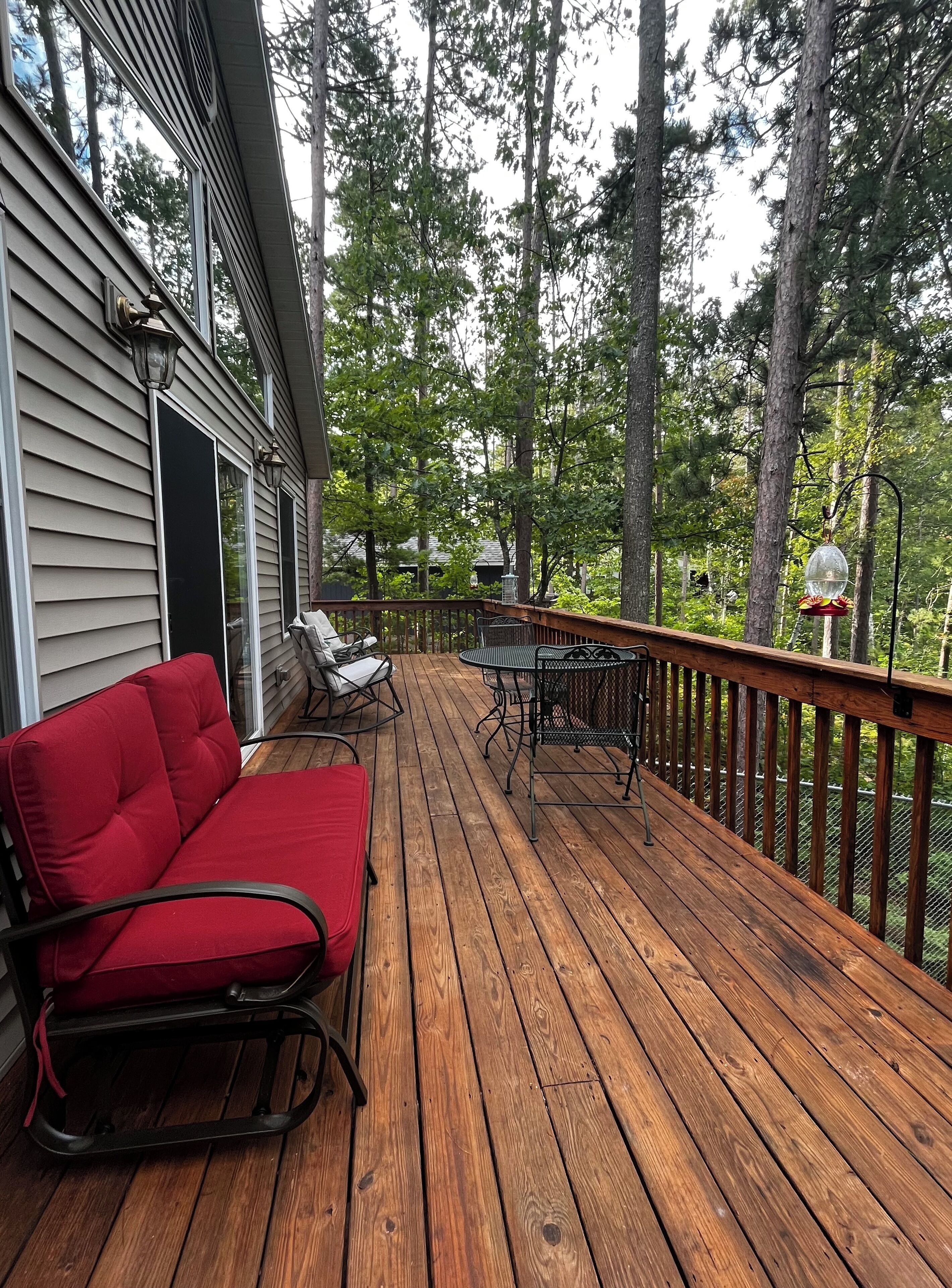 A wooden deck with a red sofa and a table, surrounded by tall trees.