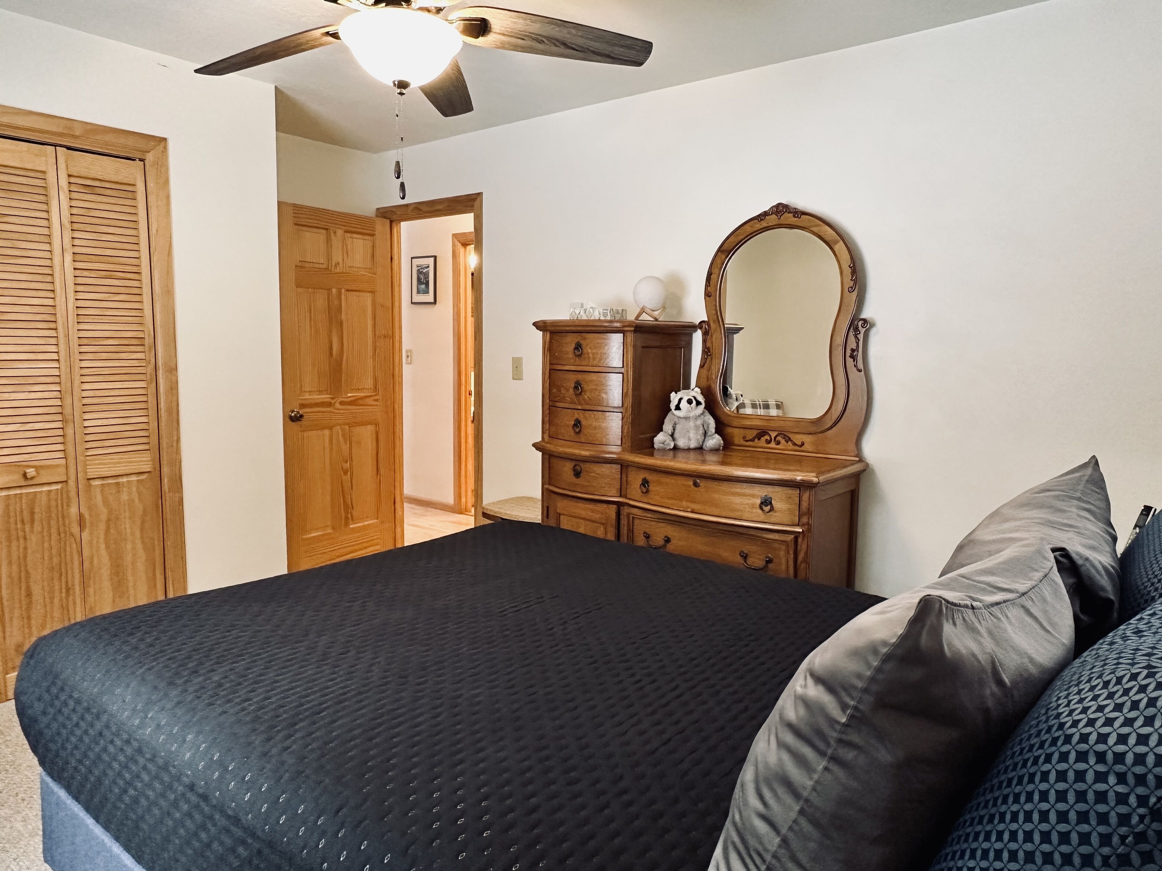 Quarto com cama, guarda-roupa de madeira, penteadeira e ventoinha no teto.
