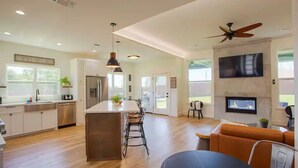 A spacious kitchen with a central island, a dining area with a round table, and a living room with a sofa and a fireplace. - The Rooftop (Denison)