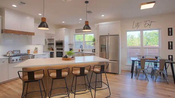 A modern kitchen with a large island, bar stools, and a dining area with a table and chairs. - The Rooftop (Denison)