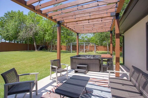 A covered patio area with outdoor furniture, a hot tub, and a pergola.