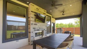 An outdoor patio with a stone fireplace, a long dining table, and wicker chairs. - The Rooftop (Denison)