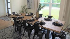 A dining area with a wooden table set for six, surrounded by black chairs. There is a vase on the table, and a painting on the wall. - The Rooftop (Denison)