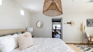 Une chambre avec un grand lit, un luminaire suspendu, un miroir et une porte donnant sur un coin repas.