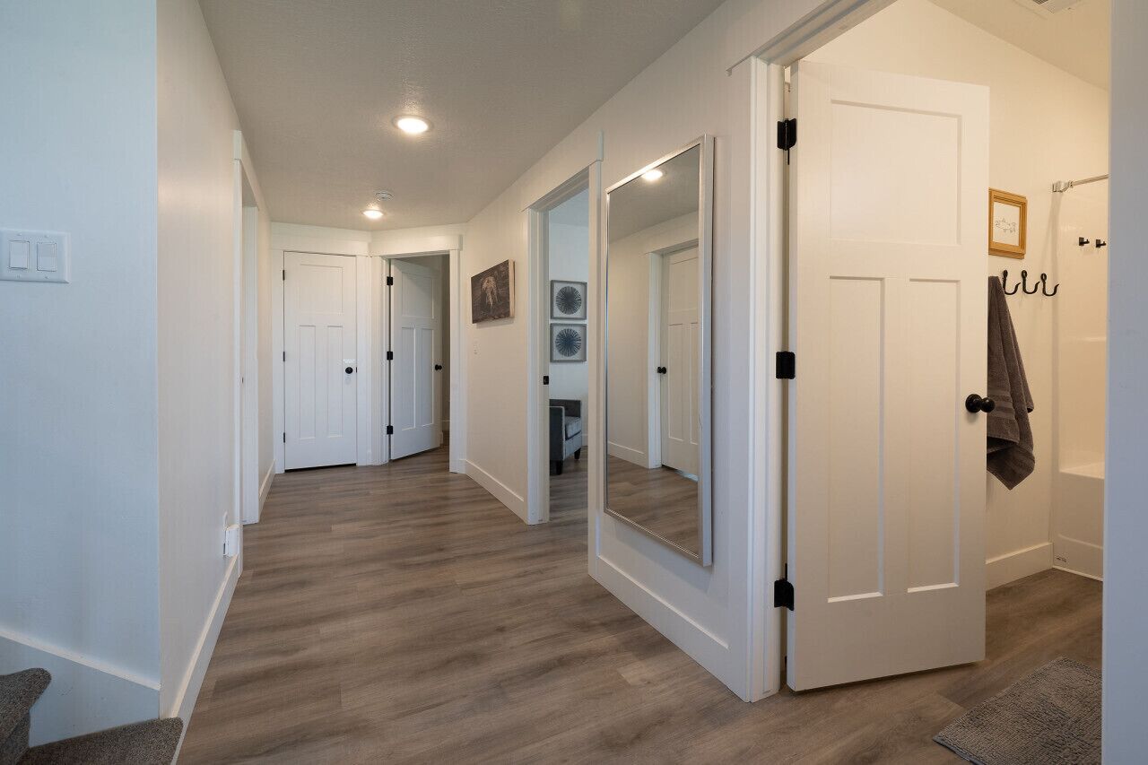 A hallway with wooden flooring, white walls, and a large mirror on one wall.