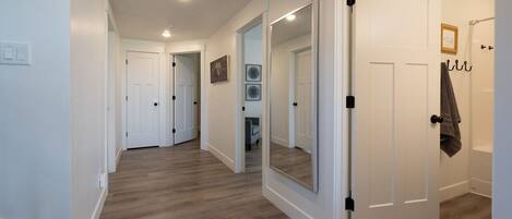 A hallway with wooden flooring, white walls, and a large mirror on one wall.