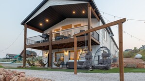 Una casa a due piani con un balcone, posti a sedere all'aperto e una sedia a dondolo.