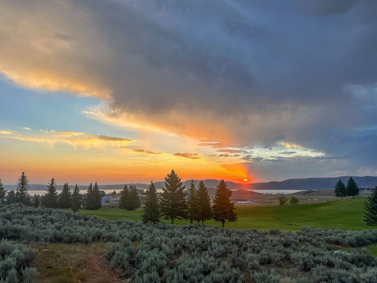 Paisaje con atardecer, árboles y una vista distante de una masa de agua.