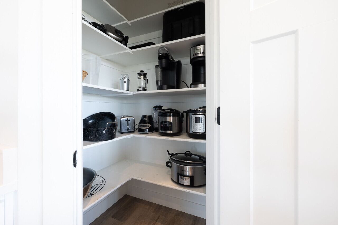 A kitchen with white shelves, various appliances including a coffee maker, toaster, and slow cooker.