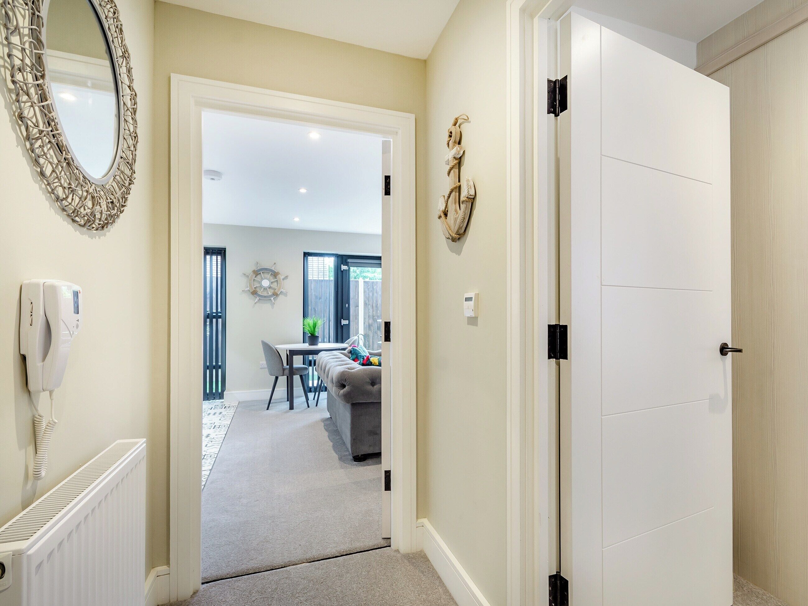 A hallway leading to a dining area with a white door, a mirror, a radiator, and a telephone.