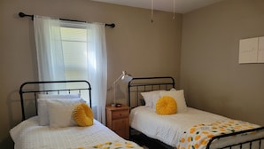 Two single beds with white bedding and yellow pillows, a bedside table with a lamp, and a window with sheer curtains. - Clean, quiet and perfectly located in the city.  Near downtown. (Columbus)