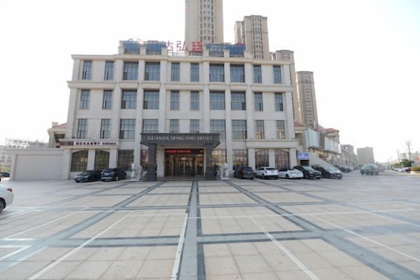 A hotel with a large entrance, multiple floors, and a parking lot in front.