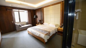 Una habitación de hotel moderna con una cama grande, un sofá, una mesita de noche y un ventanal amplio.