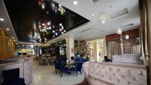 Un lobby espacioso con un techo alto, una zona de estar central con una mesa redonda y un bar al fondo.