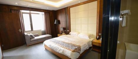 A hotel room with a large bed, a sofa, a bedside table, a lamp, and a view of the outside.