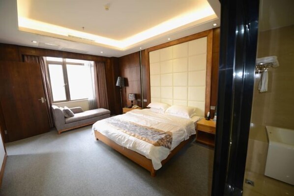 Habitación de hotel con una cama grande, un sofá, una mesita de noche, una lámpara y vistas al exterior.