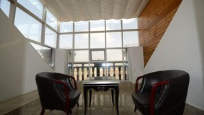 Una habitación con techo alto, ventanas amplias, dos sillas negras y una mesa.