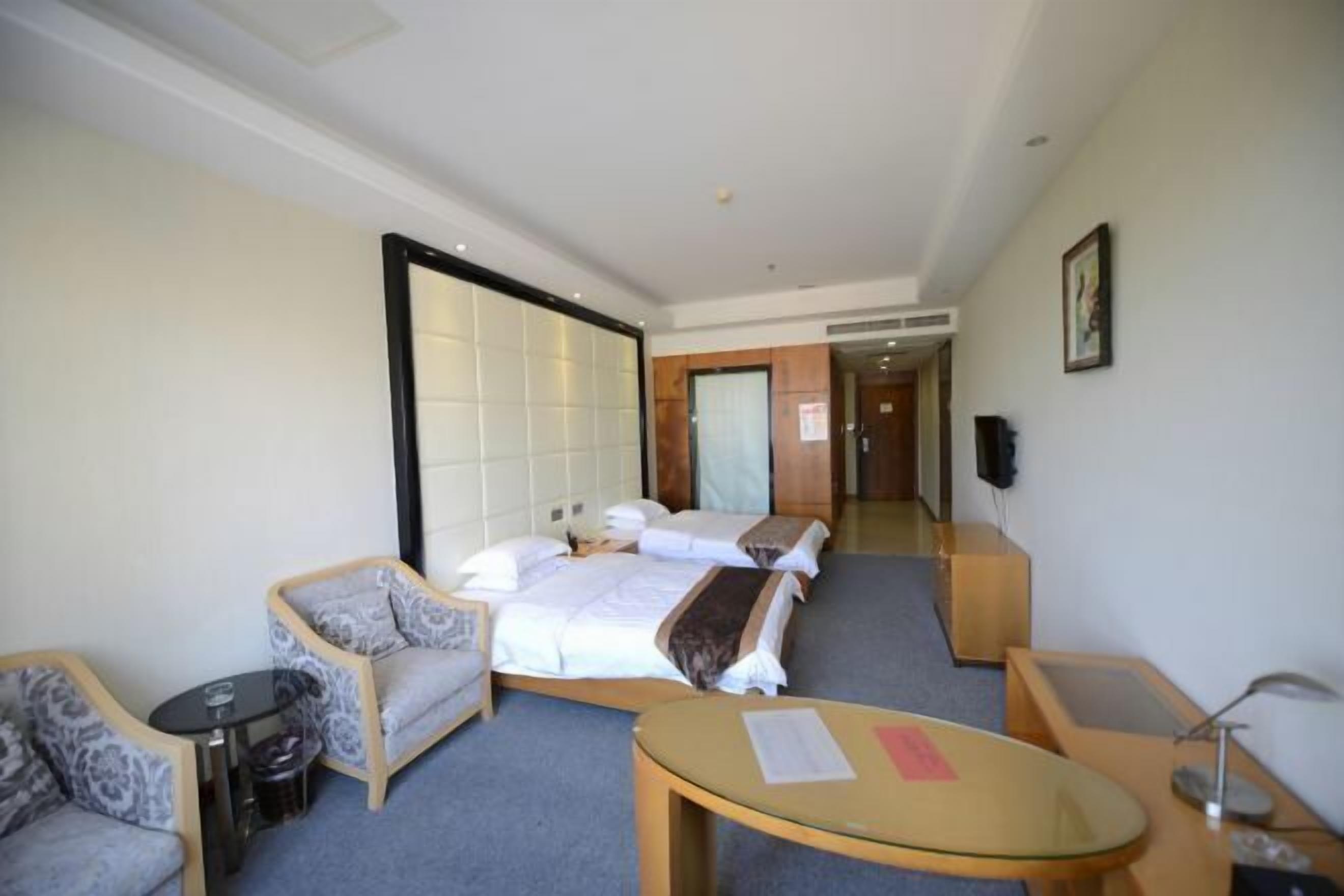 A hotel room with a bed, two armchairs, a small table, and a TV.