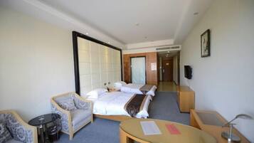 A hotel room with a bed, two armchairs, a small table, and a TV.