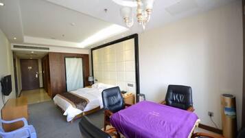 A hotel room with a bed, a desk, two chairs, a TV, and a large mirror.