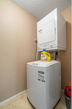 A compact laundry room with a front-loading washing machine and a stacked dryer. - Hart of it All | Top Floor | Pool | Hot Tub | Gym (Invermere)