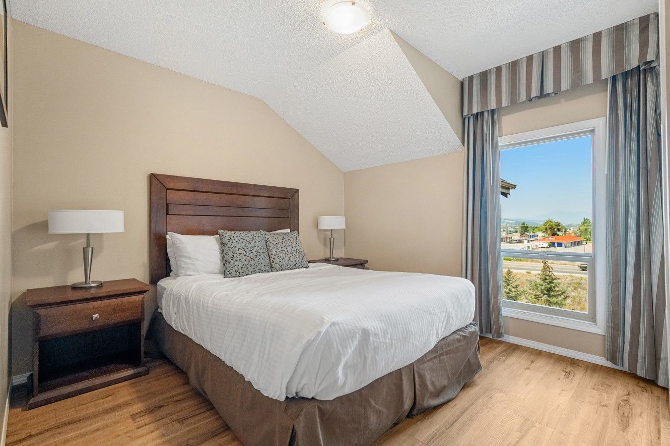 Habitación de hotel con una cama grande, dos mesitas de noche, una ventana con cortinas y vistas al exterior.
