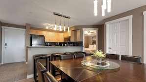 A modern kitchen with a central island, a dining area with a glass-top table, and a living space with a sofa and a TV.
