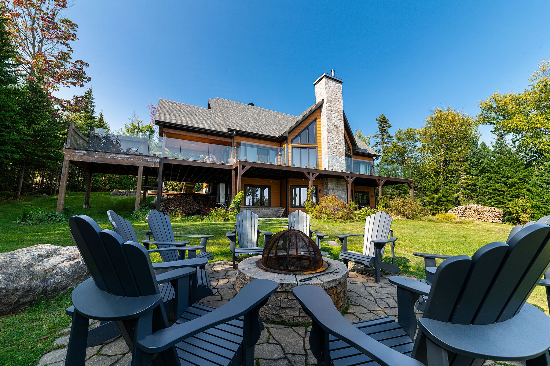 A modern house with a stone chimney, a deck with outdoor seating, and a fire pit.