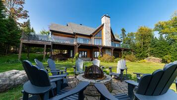 A modern house with a stone chimney, a deck with outdoor seating, and a fire pit.