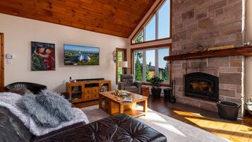 A cozy living room with a fireplace, wooden ceiling, and large windows.