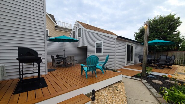 Un jardin avec une terrasse en bois, un barbecue, du mobilier d’extérieur et des parasols.