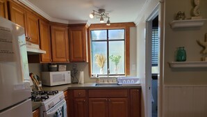 Une cuisine avec des meubles de rangement en bois, un réfrigérateur blanc, un four à micro-ondes, une cuisinière et une fenêtre ornée de plantes.