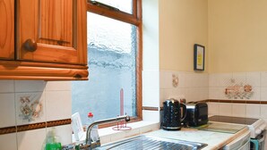 A kitchen with wooden cabinets, a stainless steel sink, a window with a view, and a tiled backsplash. - 2 bedroom accommodation in Llanrwst (Llanrwst)