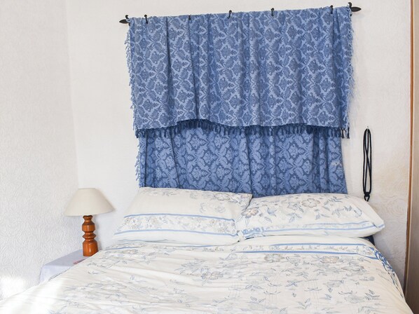 A bed with floral-patterned bedding, a blue patterned curtain, and a bedside lamp.