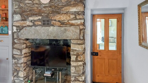 A stone fireplace with a flat-screen TV, a wooden door, and a doormat. - 2 bedroom accommodation in Llanrwst (Llanrwst)