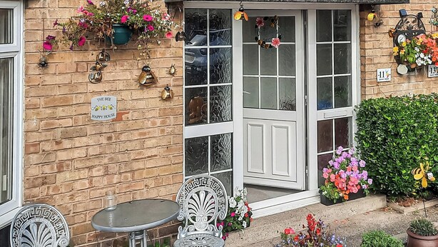 A brick building with a white door, a small table, two chairs, and various potted plants and decorations.