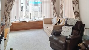 A living room with a sofa, a window with blinds, a small table, and a lamp.