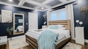A modern bedroom with a large bed, a mirror, a bedside table, and a window with curtains. - ⭐️Old 4th Ward⭐️ Designer Duplex Home - 2 Minutes from Downtown! (Atlanta)