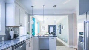 A modern kitchen with white cabinetry, a central island, pendant lighting, and a view into the dining area. - ⭐️Old 4th Ward⭐️ Designer Duplex Home - 2 Minutes from Downtown! (Atlanta)
