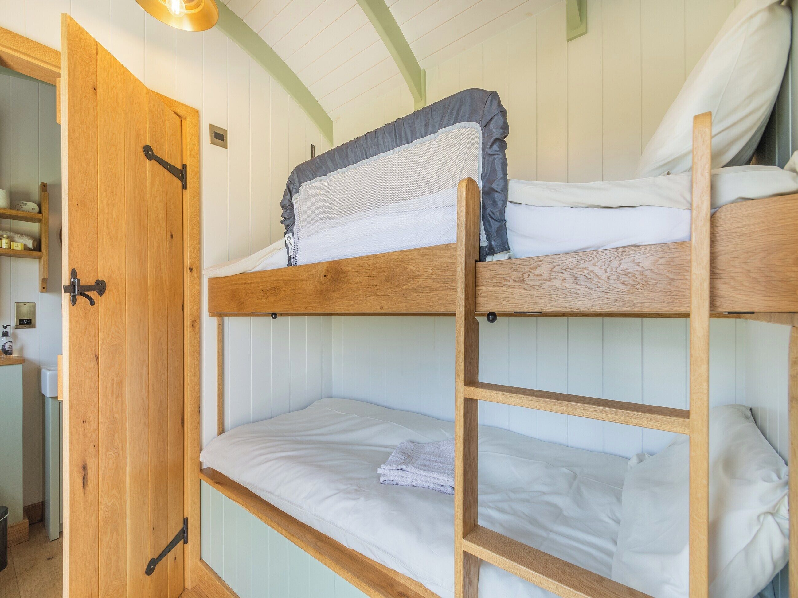 A bunk bed with a ladder, wooden walls, and a door.