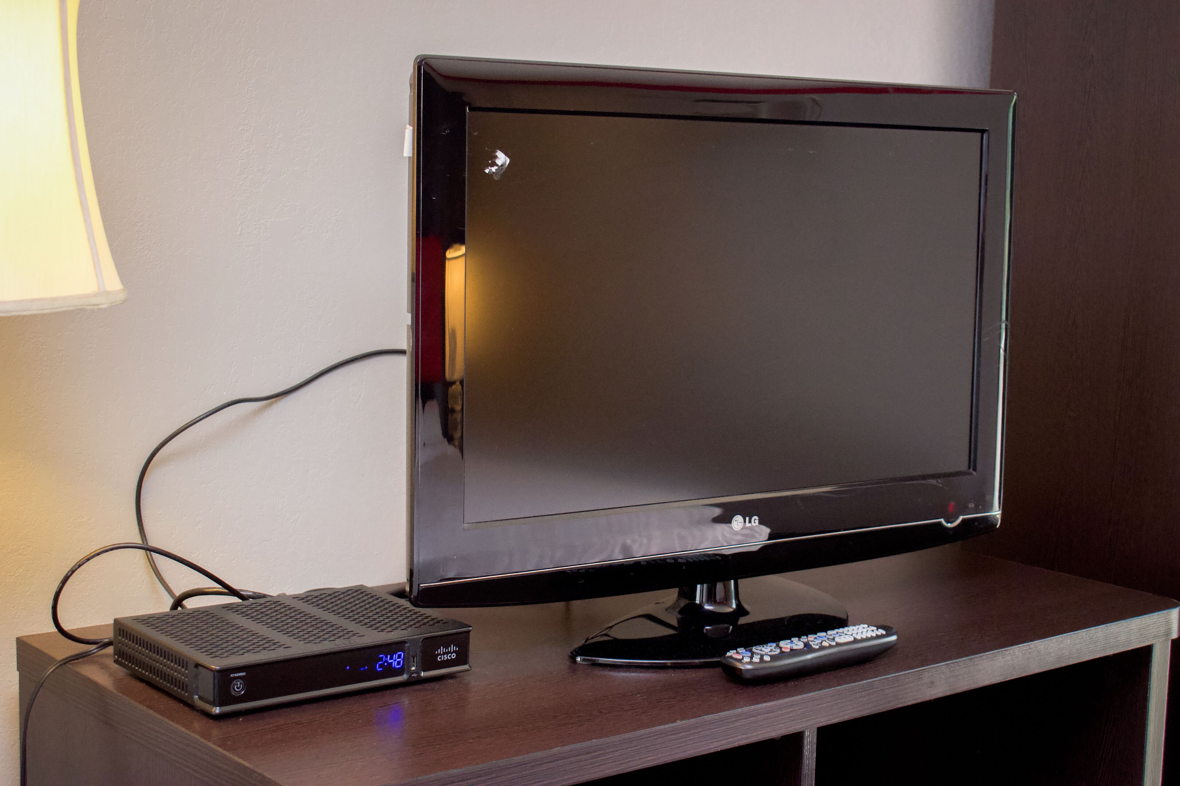 A flat-screen TV on a wooden table with a remote control and a digital clock.