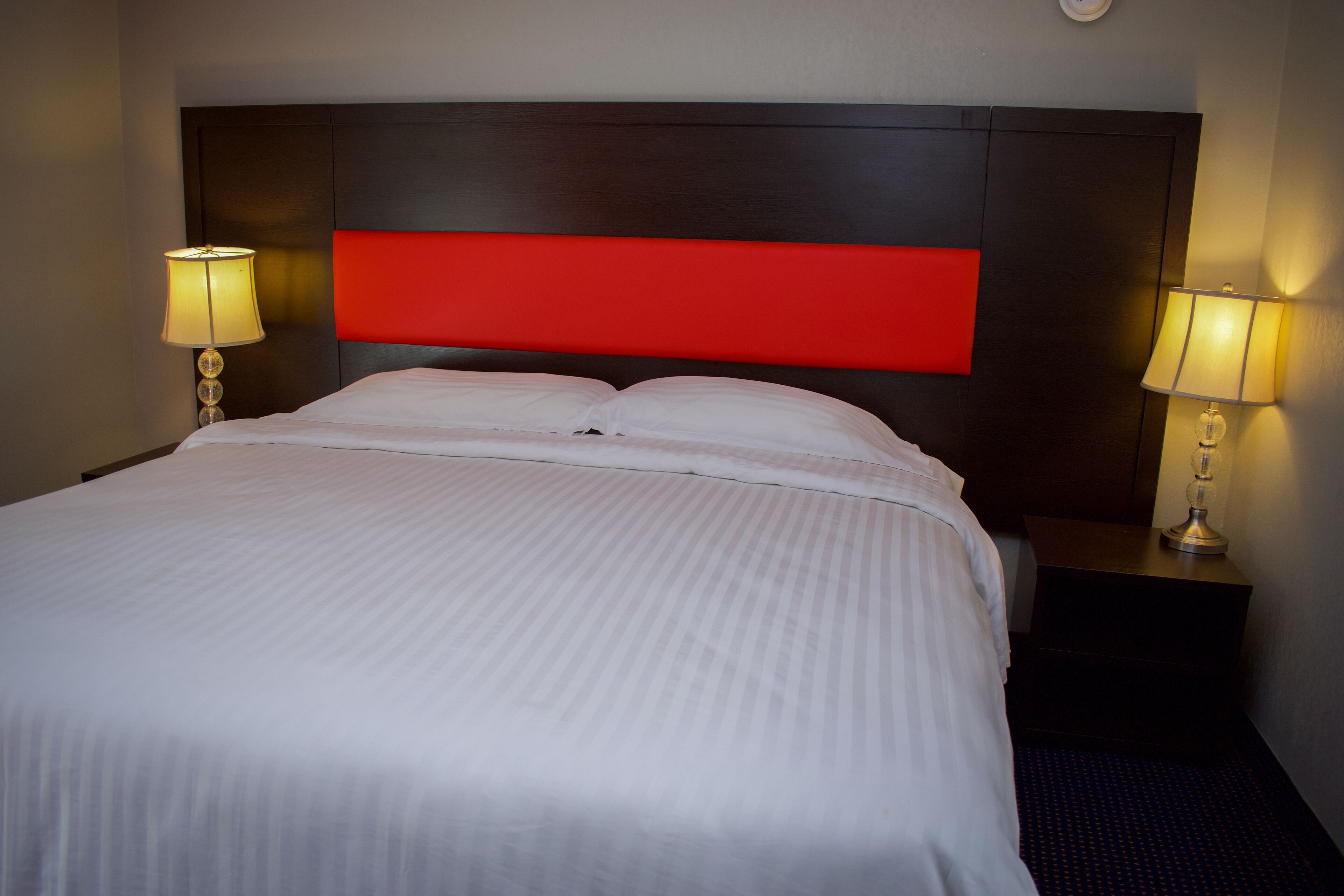 A hotel room with a large bed, two bedside lamps, and a red accent on the headboard.