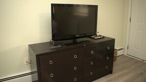 A dark wooden dresser with a flat-screen TV on top, a remote control, and a small electronic device. - Travel Inn (North Kingstown)