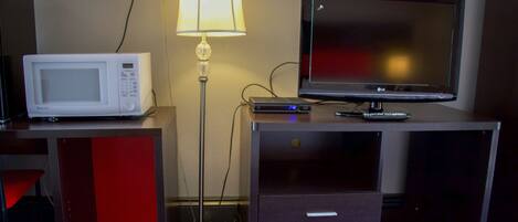 A hotel room with a microwave, a flat-screen TV, a lamp, and a desk with drawers.